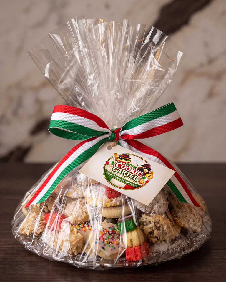 A stylized Cookie Cartel gift presentation wrapped in cellophane with tricolor ribbon and a phone-free branded tag.